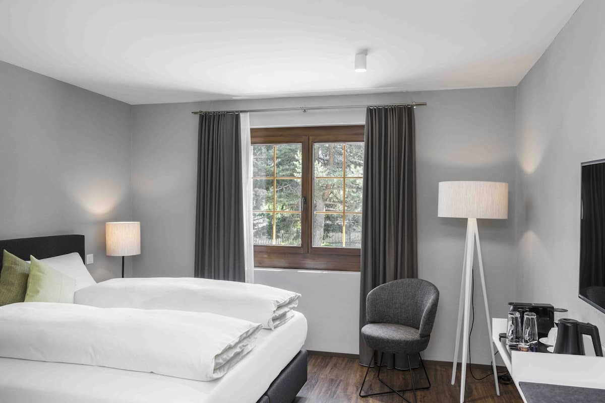A hotel room with a bed, a chair, a desk with a lamp, and a window with curtains.