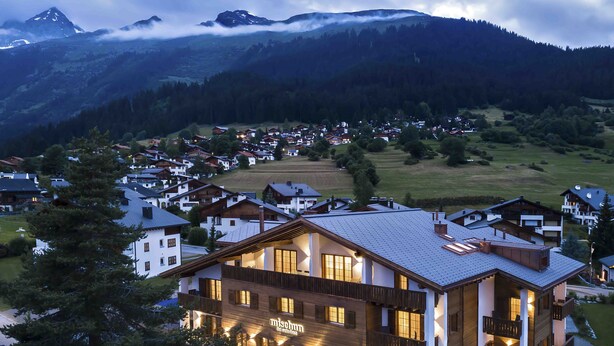 A modern hotel with a wooden facade, large windows, and a balcony overlooking a scenic mountain landscape. - Hotel mischun (Brigels)