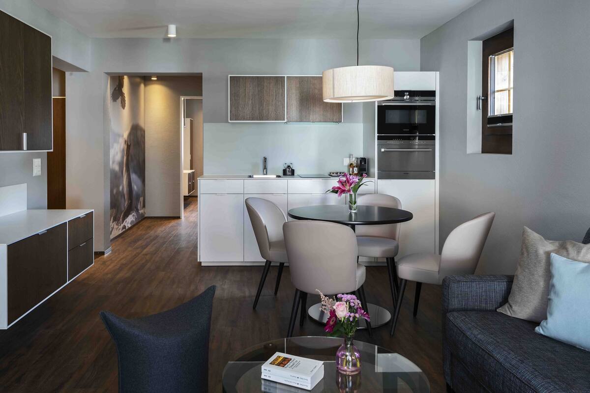 A modern living room with a glass coffee table, a sofa, and a dining area with chairs and a table.