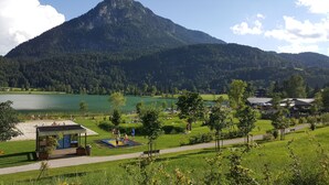 A lakeside view with a mountain in the background, a playground, and a small building with a deck. - Aparthotel Buchauer.Tirol in a natural paradise (Vorderthiersee)