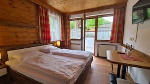 A wooden-paneled bedroom with two beds, a table with a chair, and a TV on the wall. - Aparthotel Buchauer.Tirol in a natural paradise (Vorderthiersee)