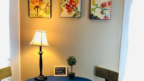 Una habitación con una mesa redonda, dos sillas, una lámpara y tres cuadros florales en la pared.