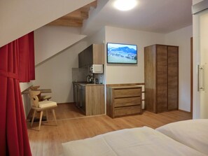 A bedroom with a bed, wooden wardrobe, and a small kitchenette.