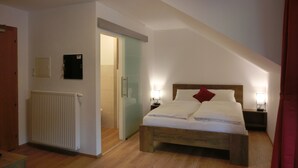 A bedroom with a sloped ceiling, a bed with white linens and a red pillow, a wooden headboard, and two bedside lamps. - Aparthotel Buchauer.Tirol in a natural paradise (Thiersee)