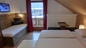 Ein gemütliches Schlafzimmer im Dachgeschoss mit holzgetäfelter Schräge, einem großen Fenster mit roten Vorhängen, einem Fernseher an der Wand und einem kleinen Tisch mit Lampe.