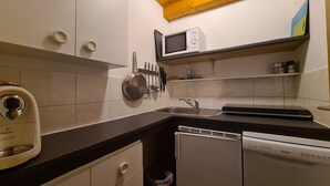 Eine kompakte Küche mit weißen Schränken, einer schwarzen Arbeitsplatte, einer Mikrowelle, einem Geschirrspüler und einer Kaffeemaschine.