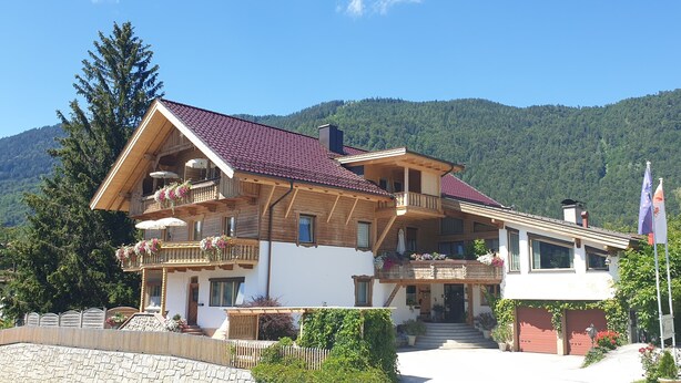 Ein Chalet mit mehreren Balkonen, einem roten Ziegeldach und einer Fahnenstange.