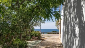 A pathway leading to a beach with a view of the sea, surrounded by greenery and a white building.