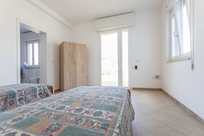A bedroom with two beds, a wardrobe, a door leading to a balcony, and a window.