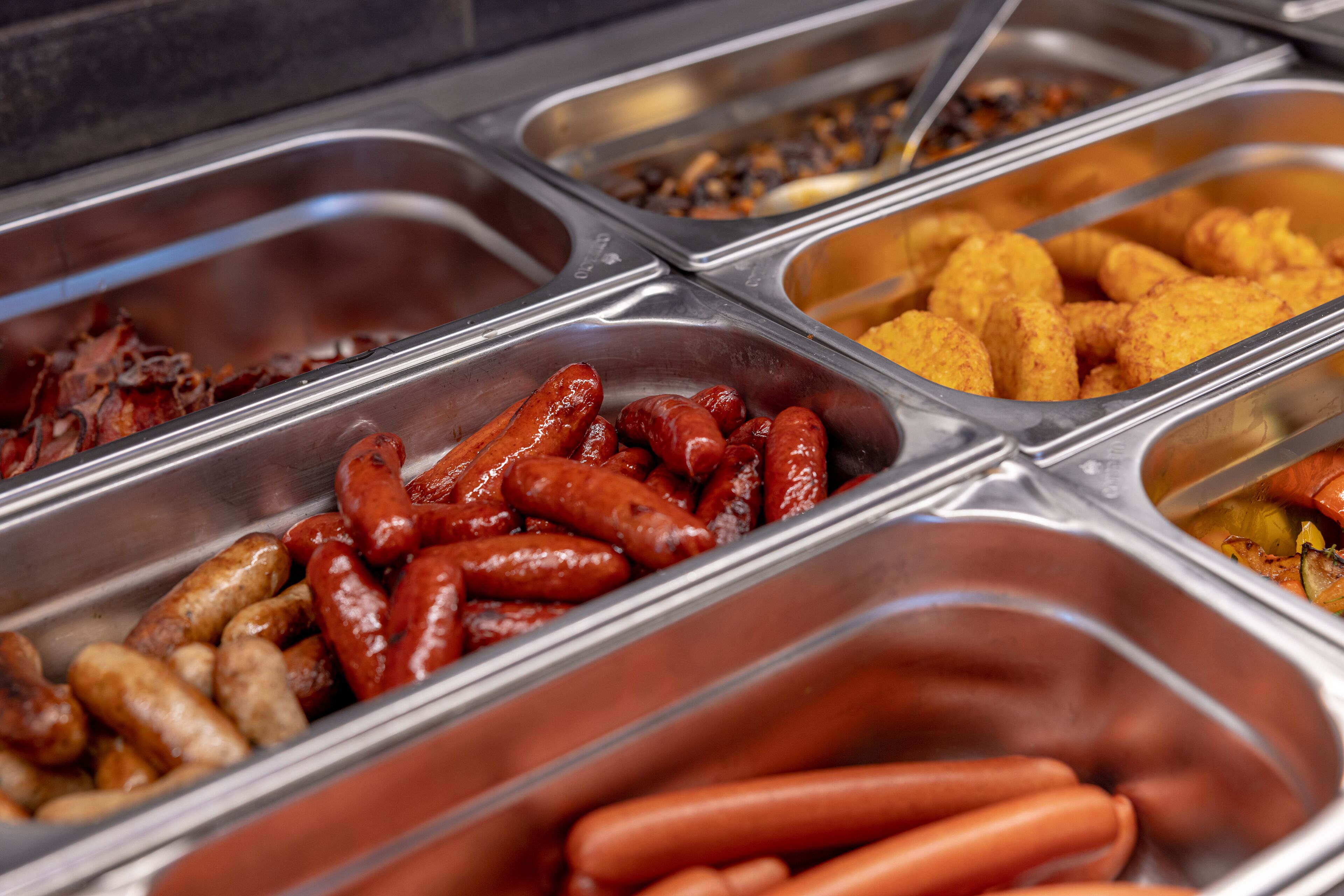 A buffet with various food options including sausages, tater tots, and other snacks.