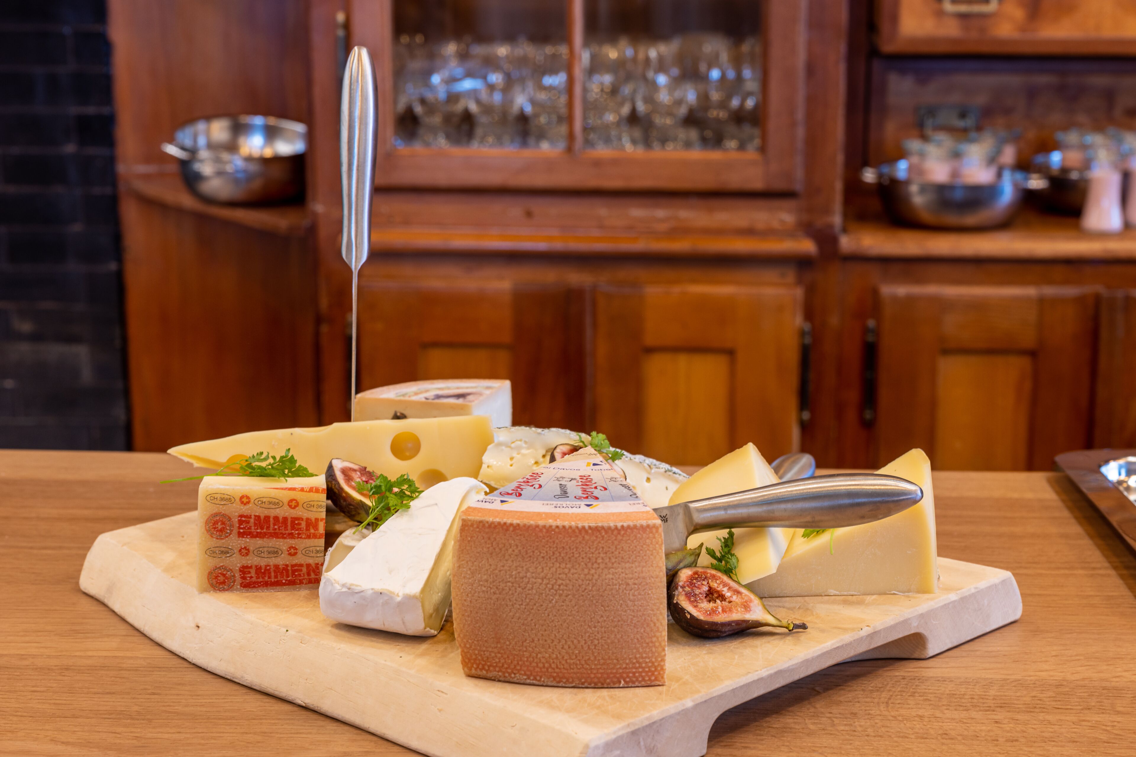 A variety of cheeses on a wooden board in a kitchen setting.