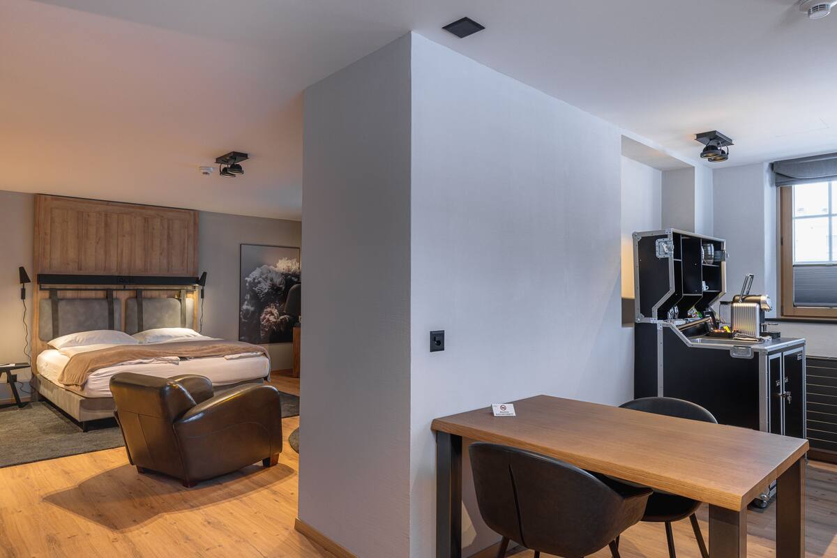 Habitación de hotel compacta con cama, sofá, escritorio y kitchenette.