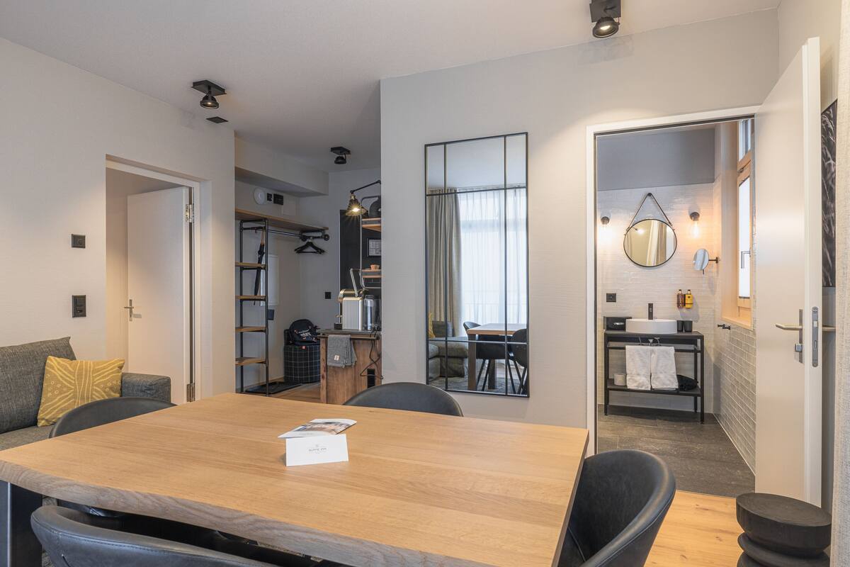 Una habitación de hotel moderna con una mesa de comedor de madera, un sofá y un área de baño separada.