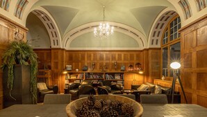 A library with wooden paneling, bookshelves, leather chairs, and a large wooden table with a pinecone centerpiece. - ALPINE INN Davos (Davos)