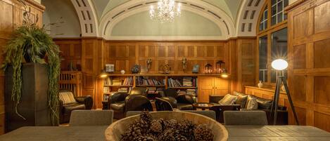 Una biblioteca con paneles de madera, estanterías, sillones de cuero y una gran mesa de madera con un centro de piñas.