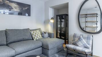 Un salon avec un canapé gris, un fauteuil assorti, une table basse, une bibliothèque et un grand miroir au mur.