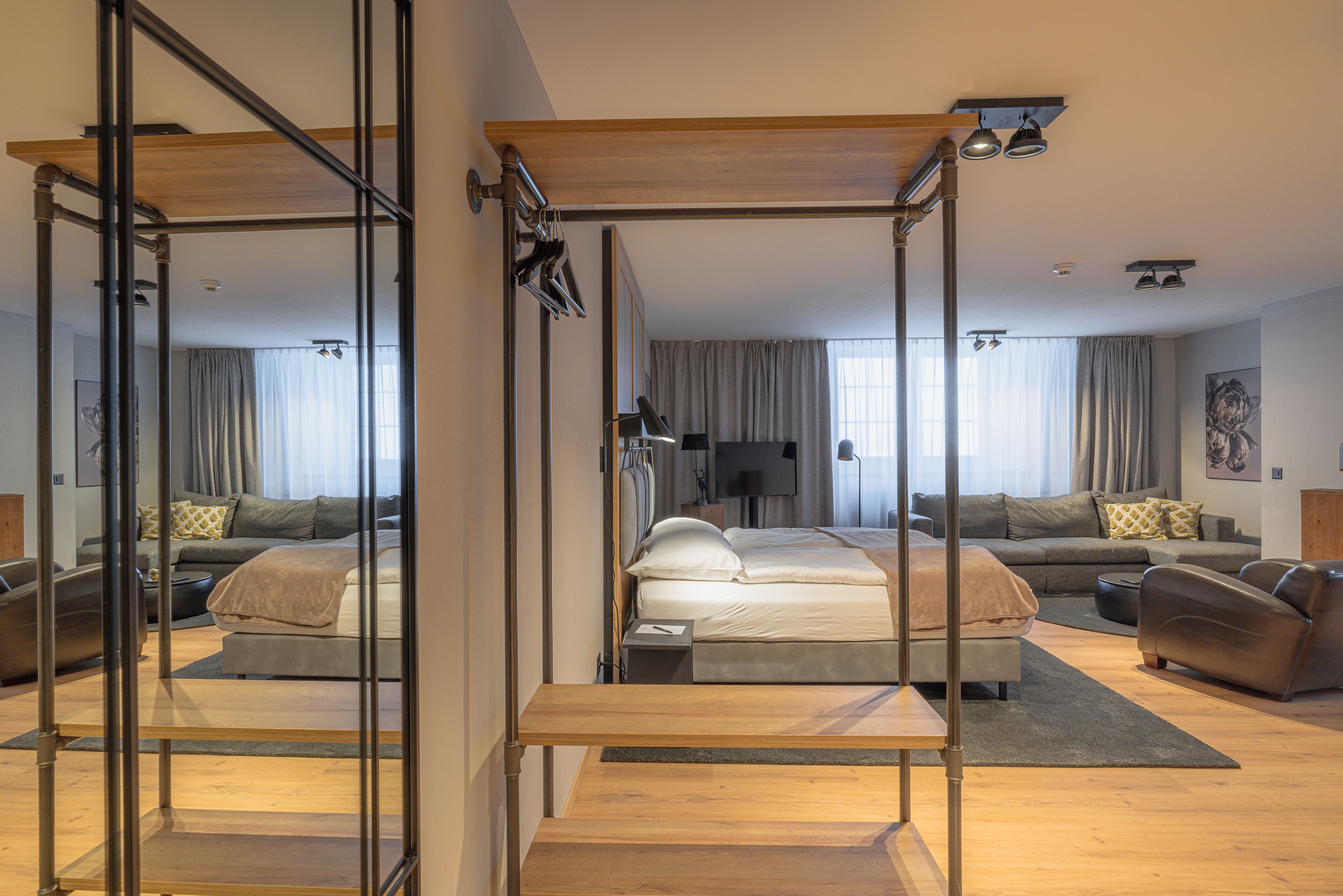 A modern hotel room with a bed, a sofa, a TV, and a large mirror.