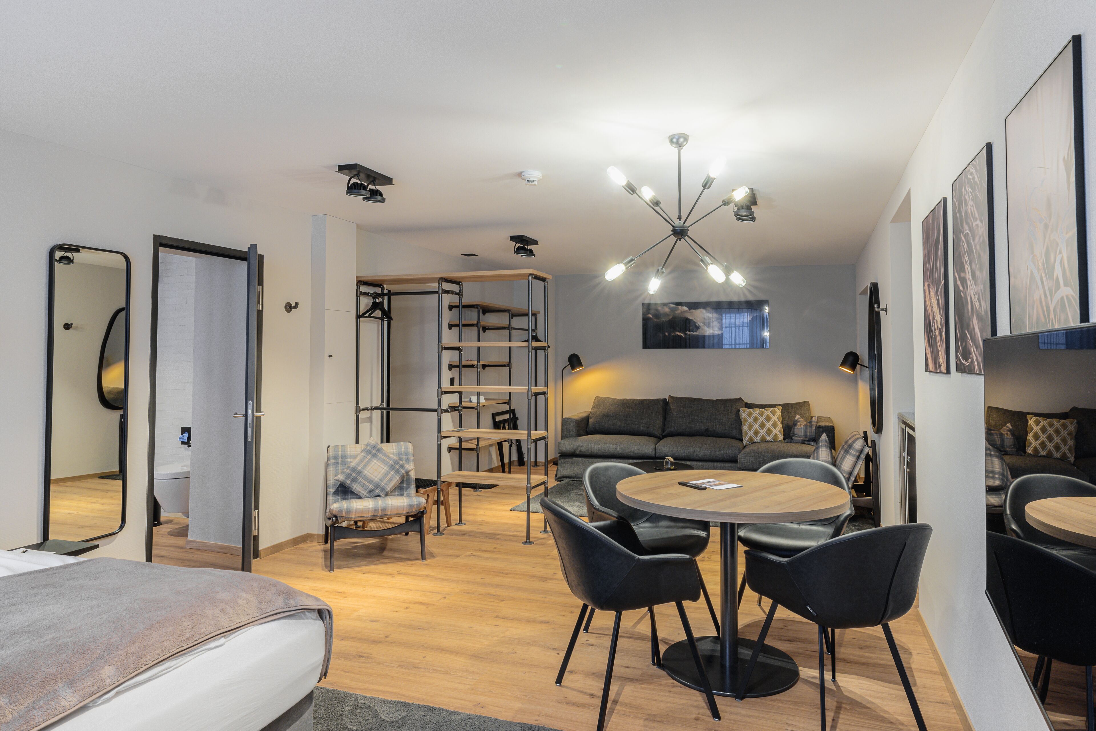 Una habitación moderna y bien iluminada con una cama, una mesa de comedor con sillas, un sofá y una estantería.