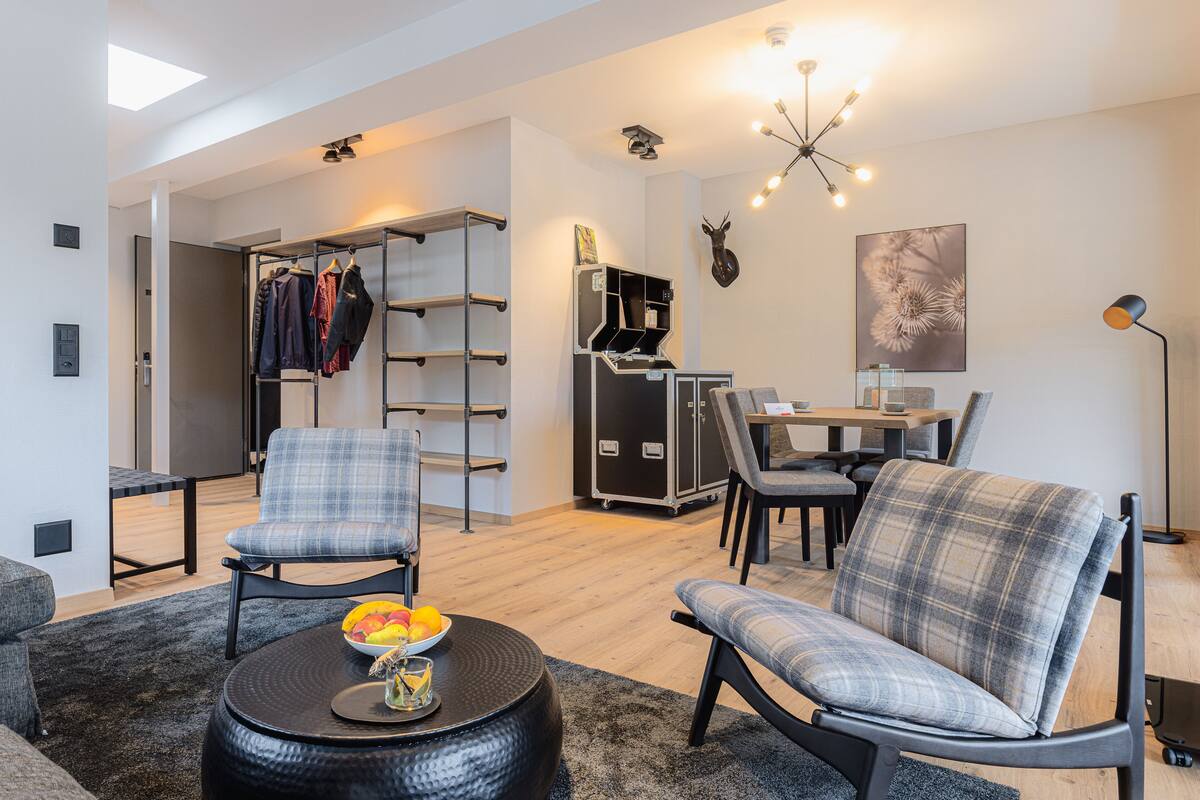 Una sala de estar moderna con un sofá, sillones, una mesa de centro y un comedor con mesa y sillas. Hay un perchero con ropa colgada, un mueble de almacenaje y una cabeza de ciervo montada.