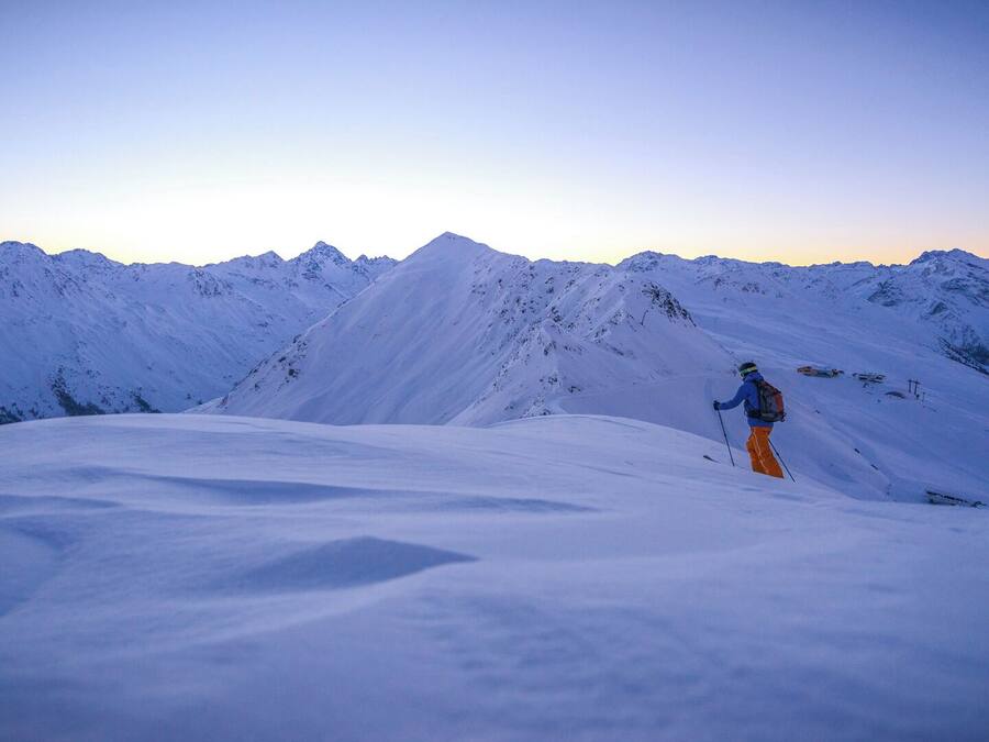 A person skiing on a snow-covered mountain slope with a clear sky.