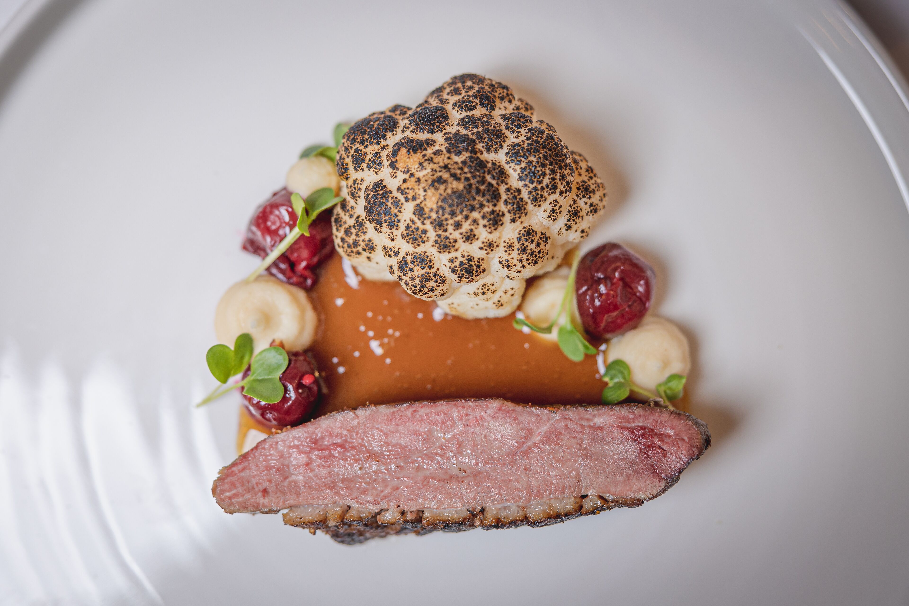 A plated dish with a piece of meat, a round bread-like item, and some berries.