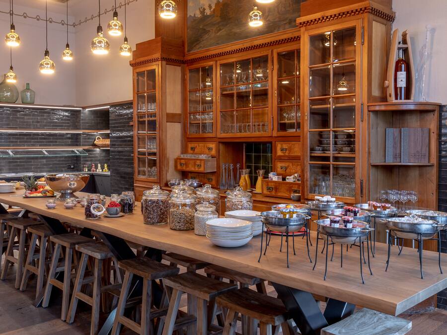 A long communal dining table with stools, surrounded by wooden cabinets with glass doors containing kitchenware.