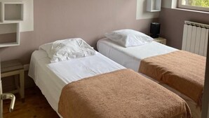 Une chambre avec deux lits, des poutres en bois, une fenêtre et des lampes fixées au mur.
