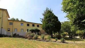 Un bâtiment jaune doté de nombreuses fenêtres et d’un jardin avec des arbres et des arbustes.