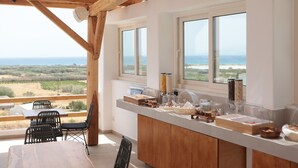 Un comedor con una mesa y sillas de madera, un mostrador de buffet con alimentos, y ventanas amplias que ofrecen vistas del paisaje.