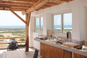 Un comedor con una mesa y sillas de madera, un mostrador de buffet con alimentos, y ventanas amplias que ofrecen vistas del paisaje.
