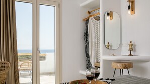 Un dormitorio con cama, una bandeja de madera con fresas y copas de vino, un espejo, un taburete de madera pequeño y vistas al mar a través de una puerta corredera.