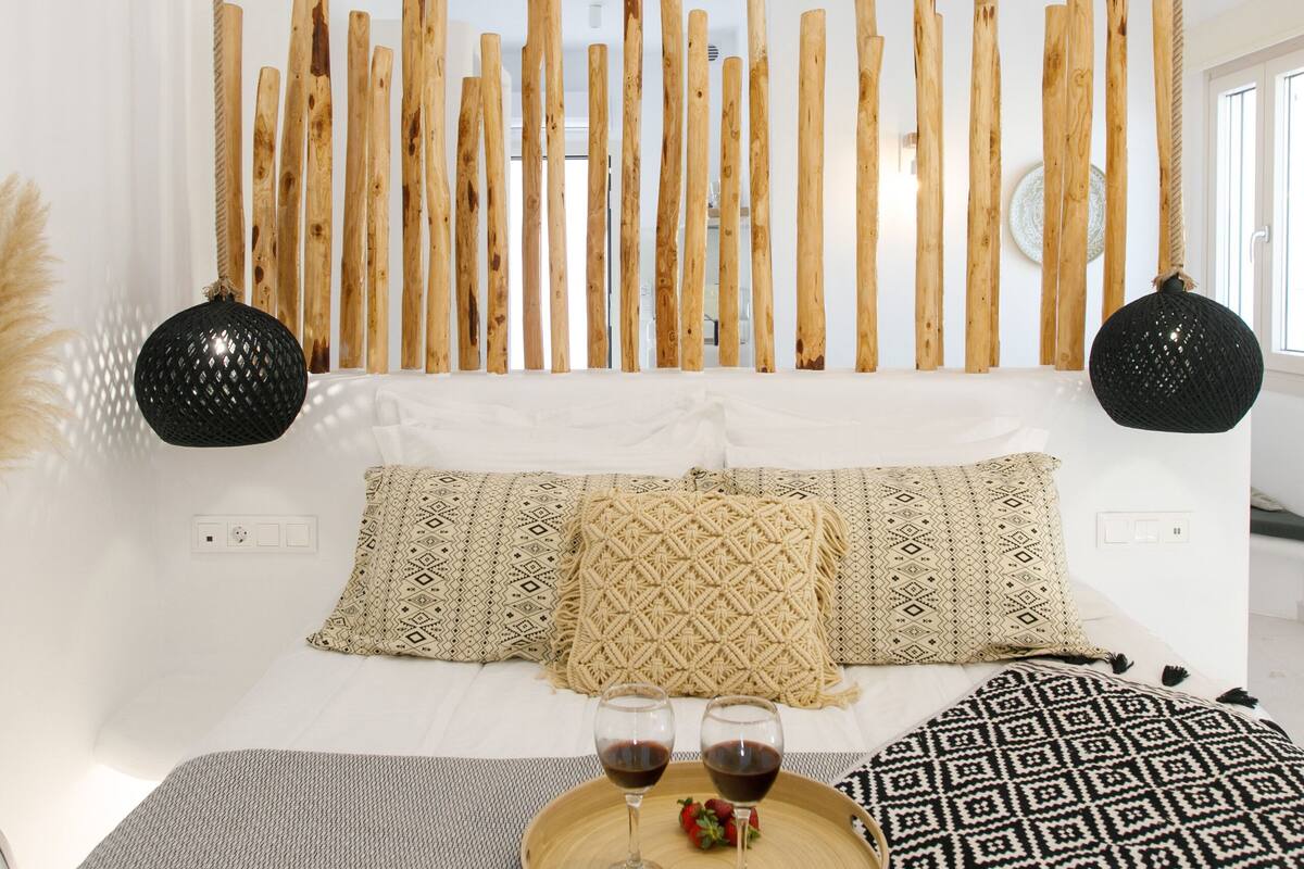 A bedroom with a bed, wooden slats, two black lamps, and a tray with glasses and a drink.