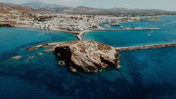 Vue aérienne d’une ville côtière, avec une formation rocheuse imposante au premier plan, un port de plaisance rempli de bateaux et une ville densément bâtie aux bâtiments blancs.
