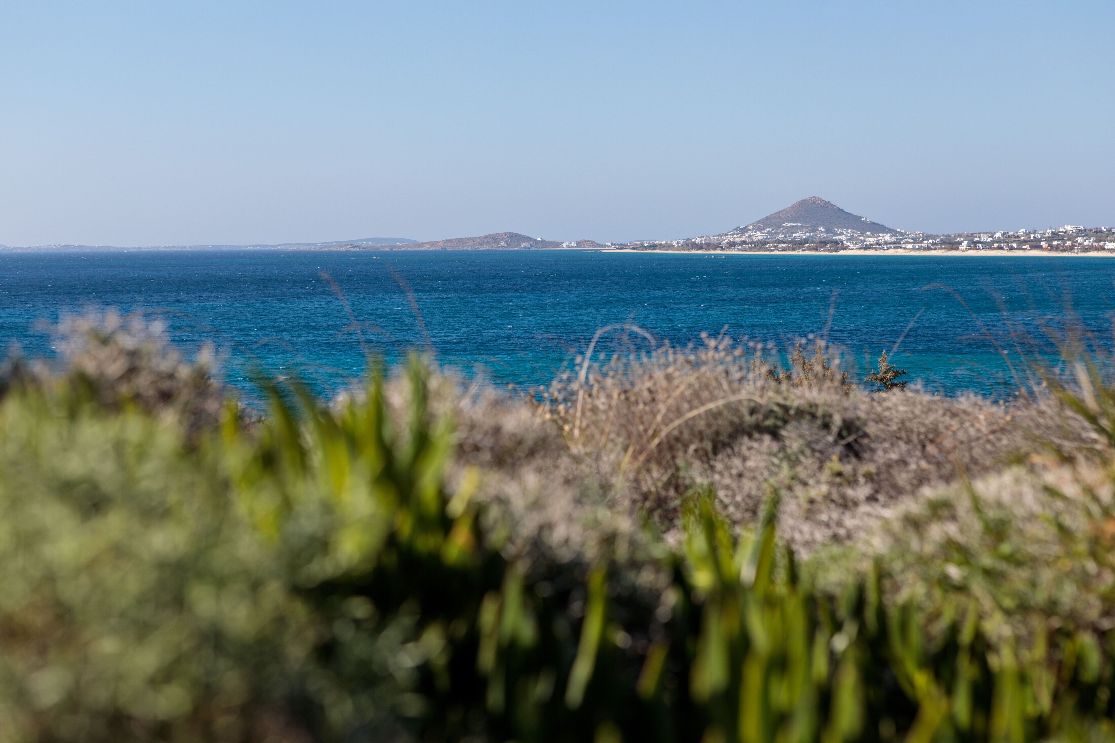 A coastal landscape with a mountain in the distance and a clear blue sea.