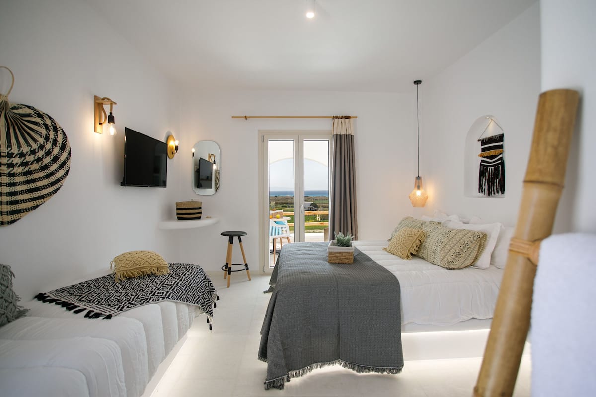 A modern bedroom with a bed, two bedside tables, a mirror, and a view through a glass door.