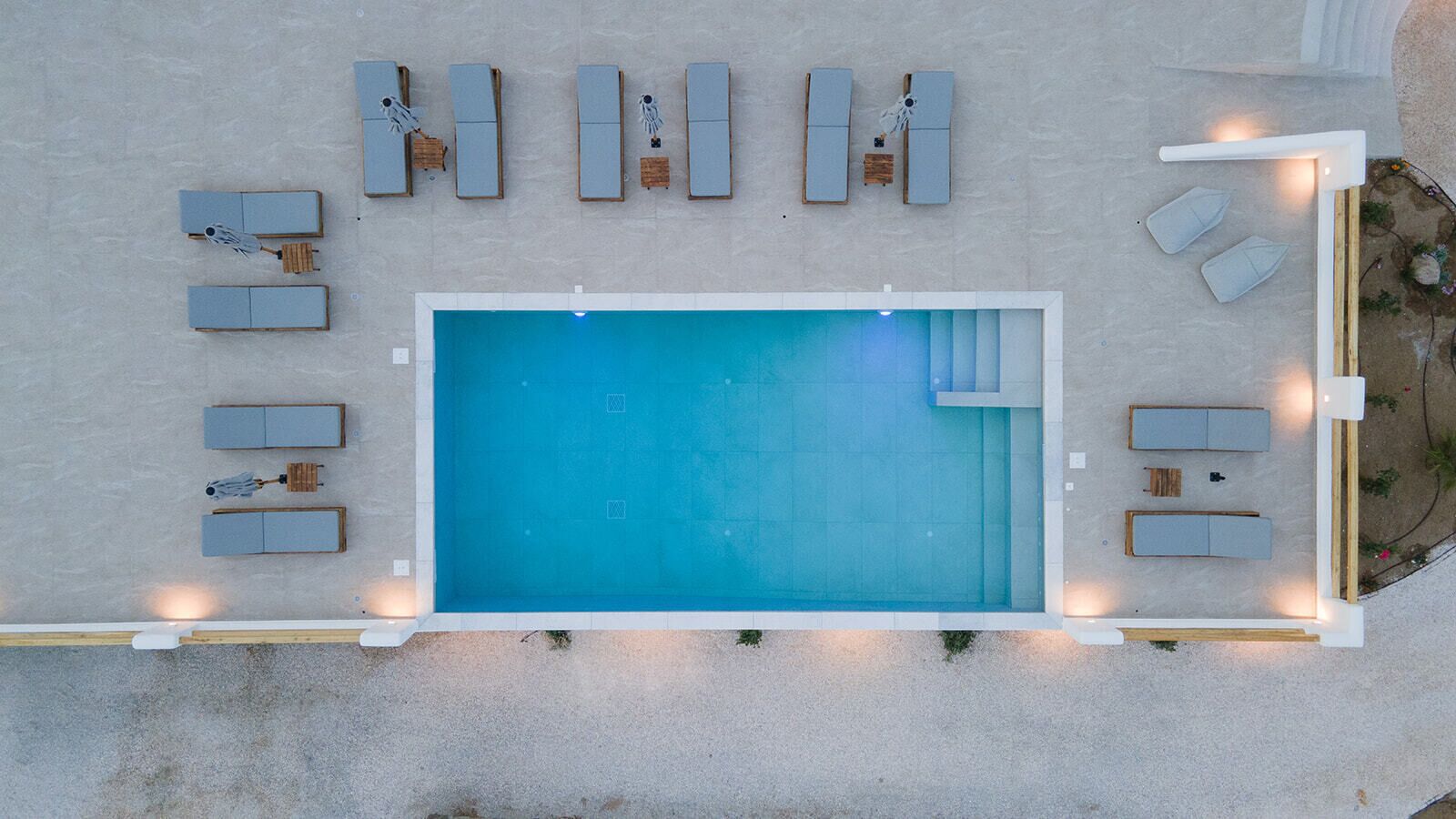 An aerial view of a swimming pool area with multiple lounge chairs and sunbeds arranged around the pool.