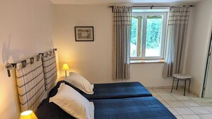 Ein Zimmer mit zwei Betten, einem Vorhangfenster, einem kleinen Hocker und einem Wandbild.