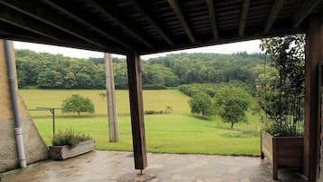 Un'area esterna coperta con pavimento in pietra, travi in legno e vista su un paesaggio verde.