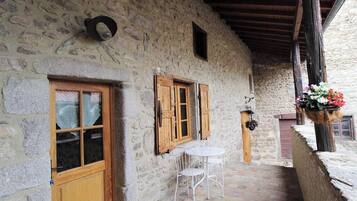 Un edificio in pietra con una porta e finestre in legno, un piccolo patio con tavolo e sedie e un cesto di fiori pensile.
