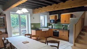 Eine Küche mit Holzschränken, einem Esstisch, Stühlen, einer Treppe und Blick ins Freie.