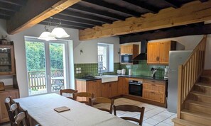 A kitchen with wooden cabinets, a dining table, chairs, a staircase, and a view of the outdoors.