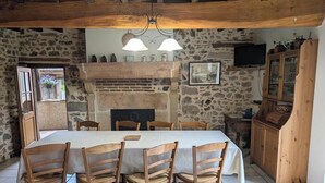 Ein rustikaler Essbereich mit Steinwand, Holzbalken an der Decke, Kamin und einem darüber montierten Fernseher.