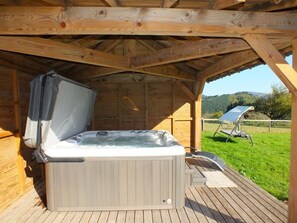 Ein Whirlpool unter einer Holzdiele mit Blick auf eine Rasenfläche und Hügel im Hintergrund.