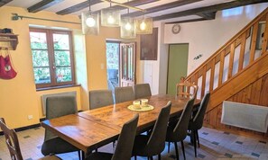 Un espace repas avec une table et des chaises en bois, un escalier et une vue sur l’extérieur.