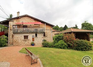 Une maison en pierre avec un balcon, une terrasse en bois et un jardin.