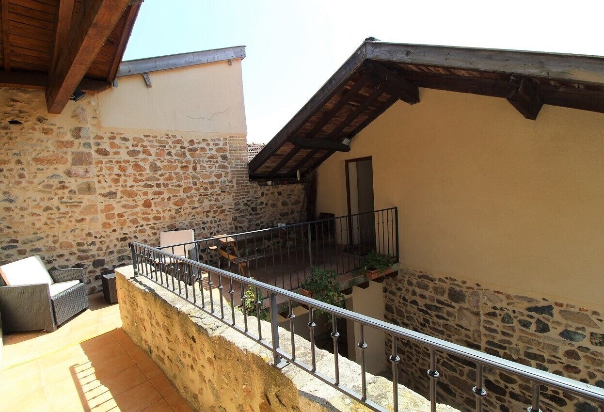 Un balcon aux murs de pierre, doté d’une rambarde en métal, de mobilier d’extérieur et de plantes en pot.