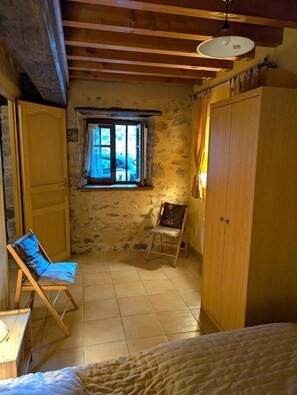 A room with a bed, a wooden wardrobe, a window with curtains, a chair, and a lamp.