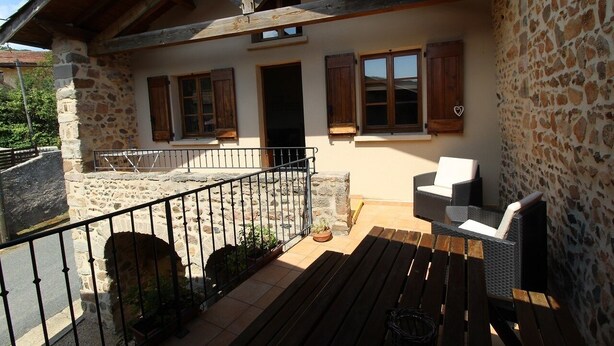 A stone building with a balcony, wooden beams, and wicker furniture.