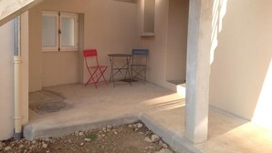 A small outdoor patio area with a concrete floor, a wooden pergola overhead, a window with a white frame, and two folding chairs. - Le gîte des Toussillards (TOUSSIEU)