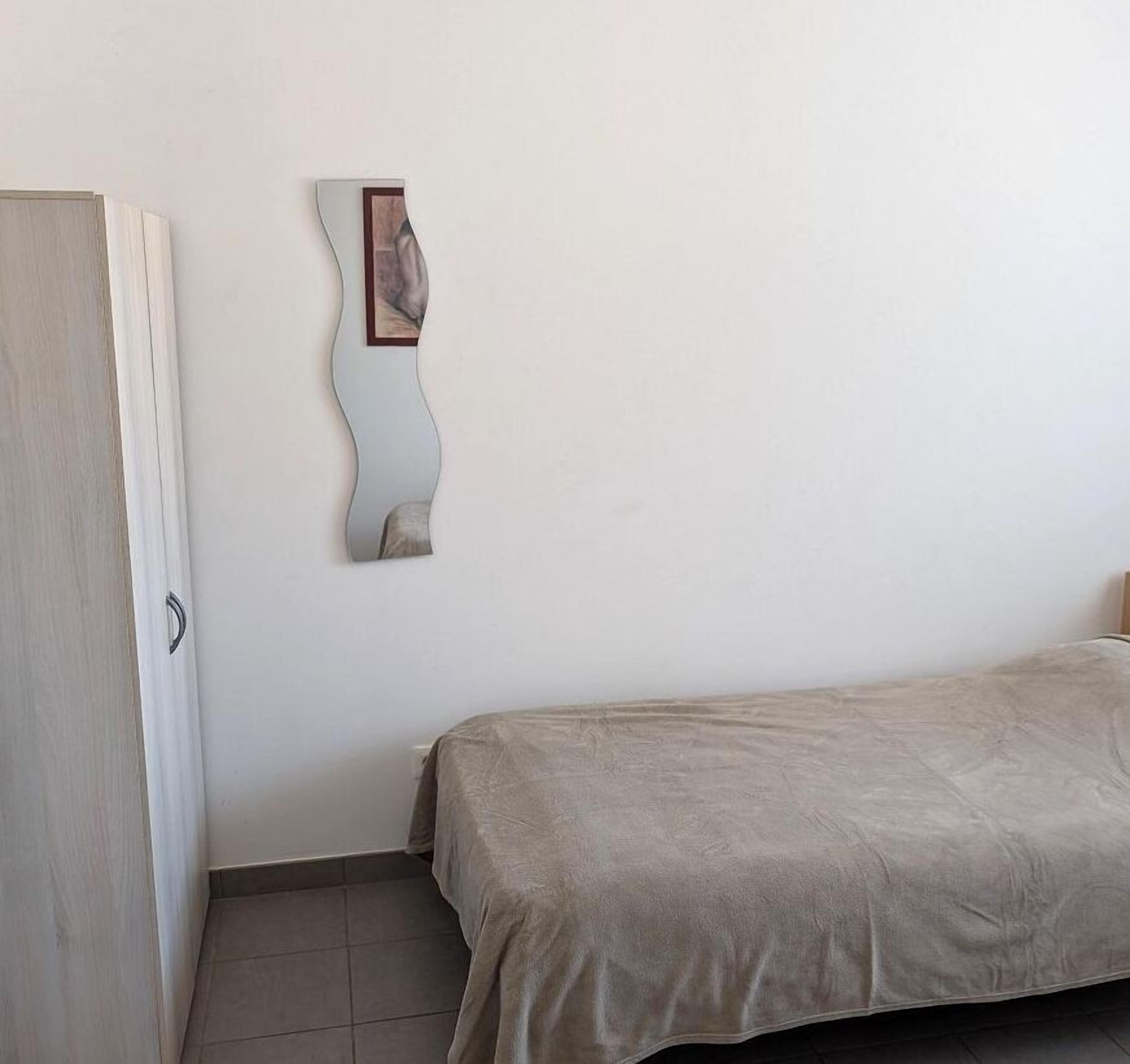 Een slaapkamer met een enkel bed, een kledingkast en een spiegel aan de muur.